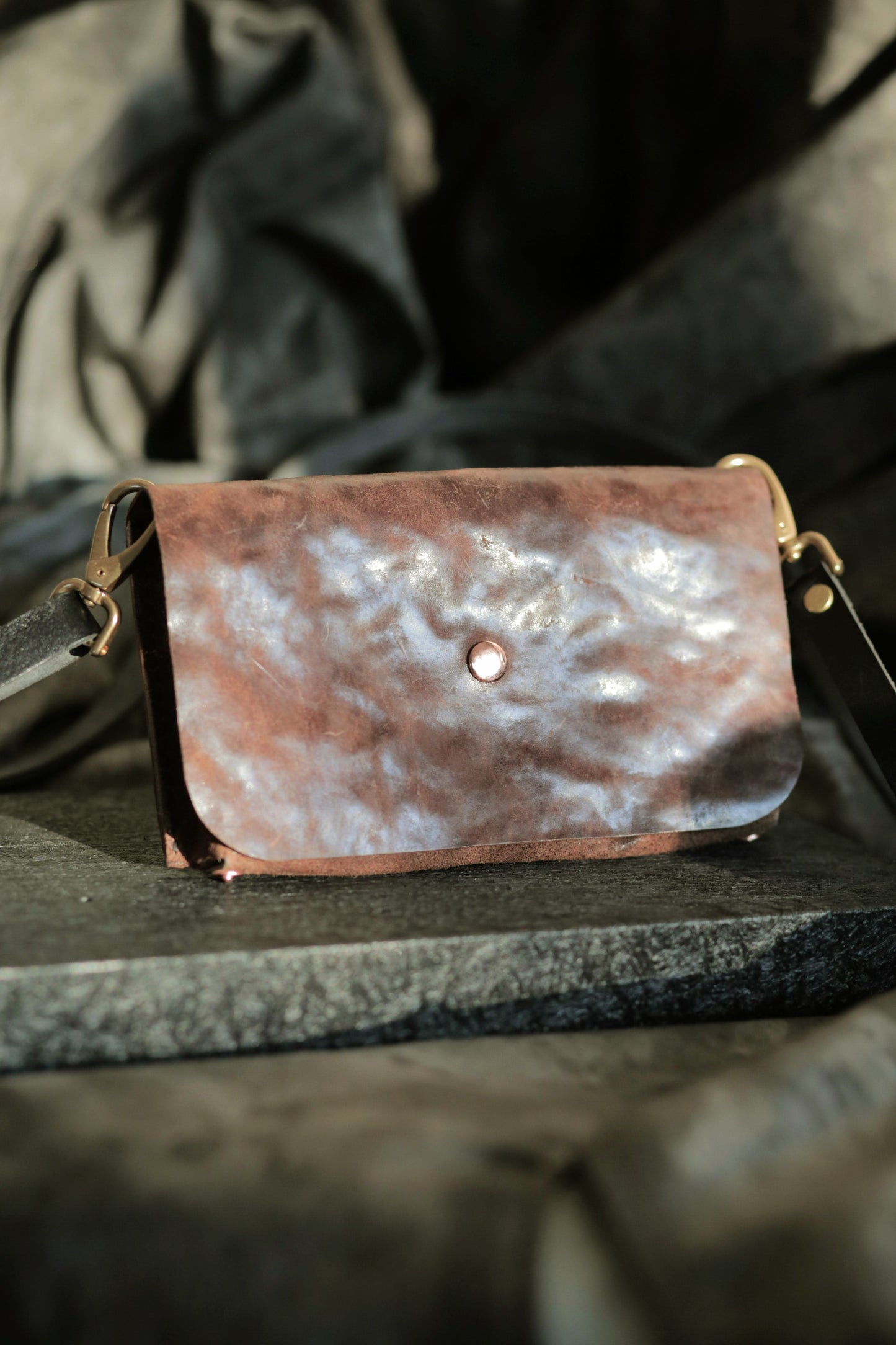 Köpenicker #003 brown bark leather clutch with copper snap and adjustable strap on dark background.