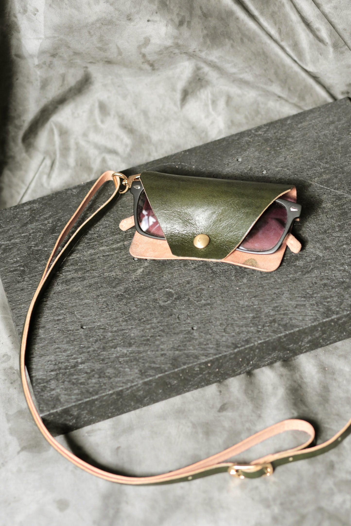 Green leather pouch with a strap on a gray surface