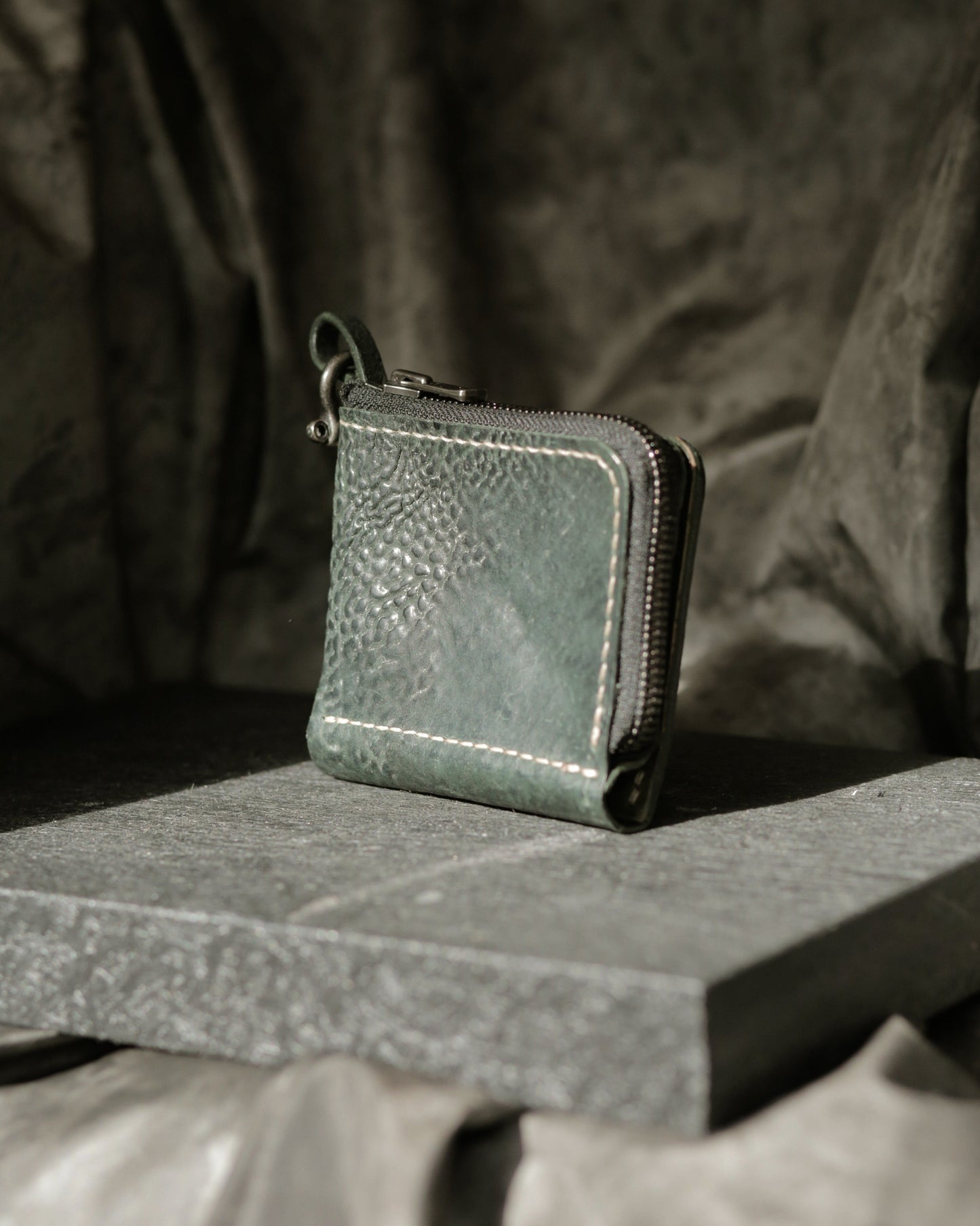 Boddin #008 new prototype handmade green leather wallet with zipper pouch and brass bow shackle on stone surface.