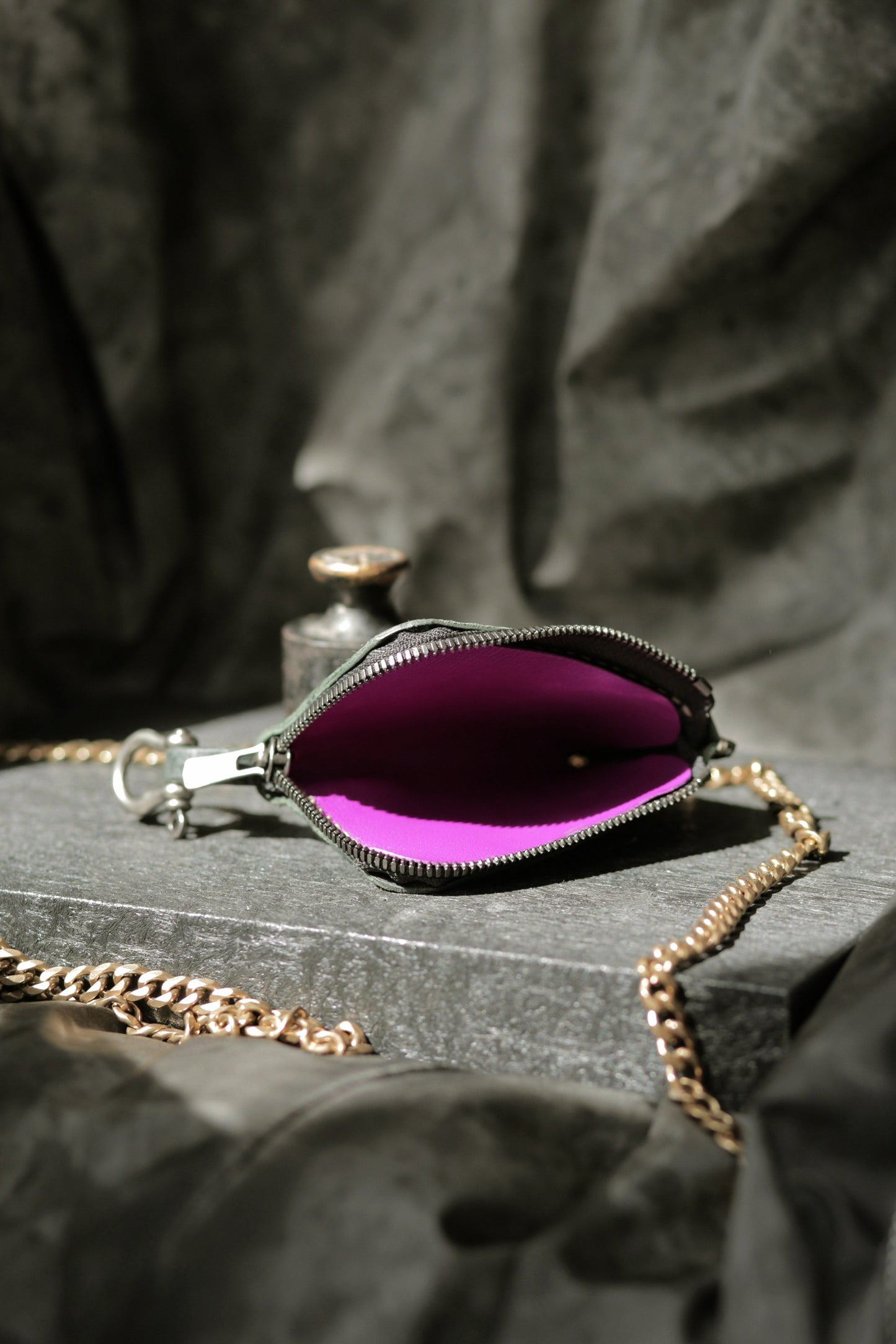 Herrfurth #002 dark green compact zip wallet with bright purple lining and brass chain on stone surface.
