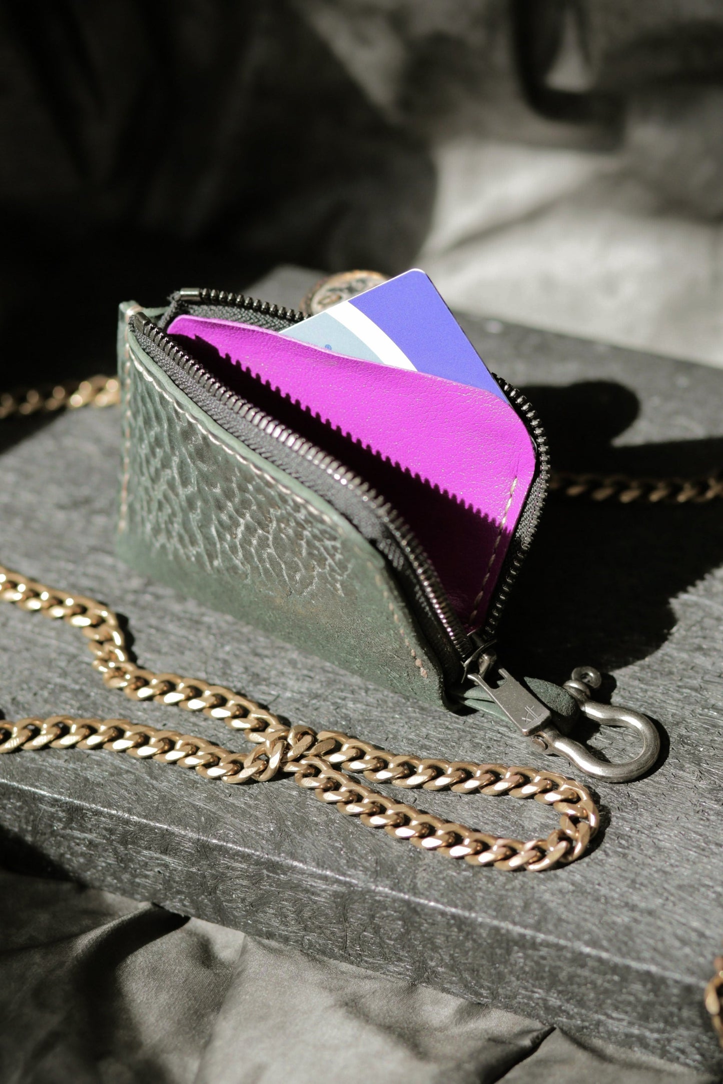 Herrfurth #002 dark green compact zip wallet with purple lining and antique brass chain on dark textured surface