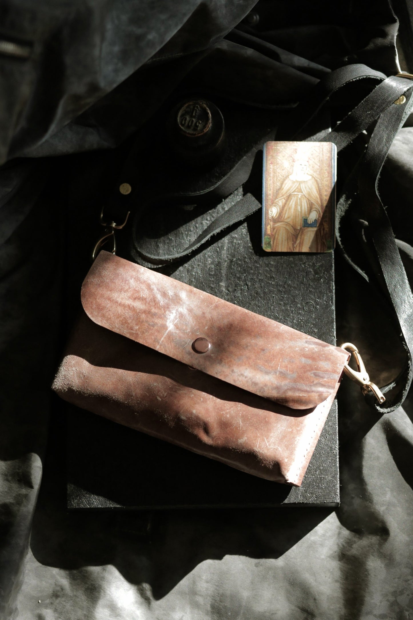 Köpenicker #002 prototype natural skin leather clutch with shoulder strap and brass hardware on dark fabric background