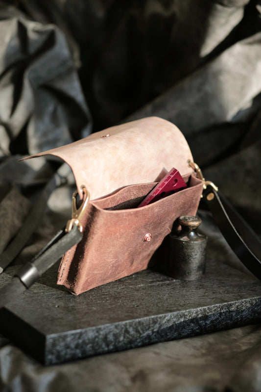 Köpenicker #003 brown bark leather clutch with adjustable strap and brass hardware open on dark textured surface.