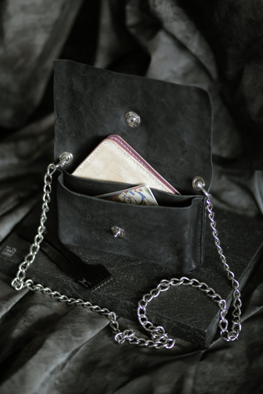 Köpenicker #004 black leather bag with polished steel chain strap, open with wallet and cash inside on dark fabric background.