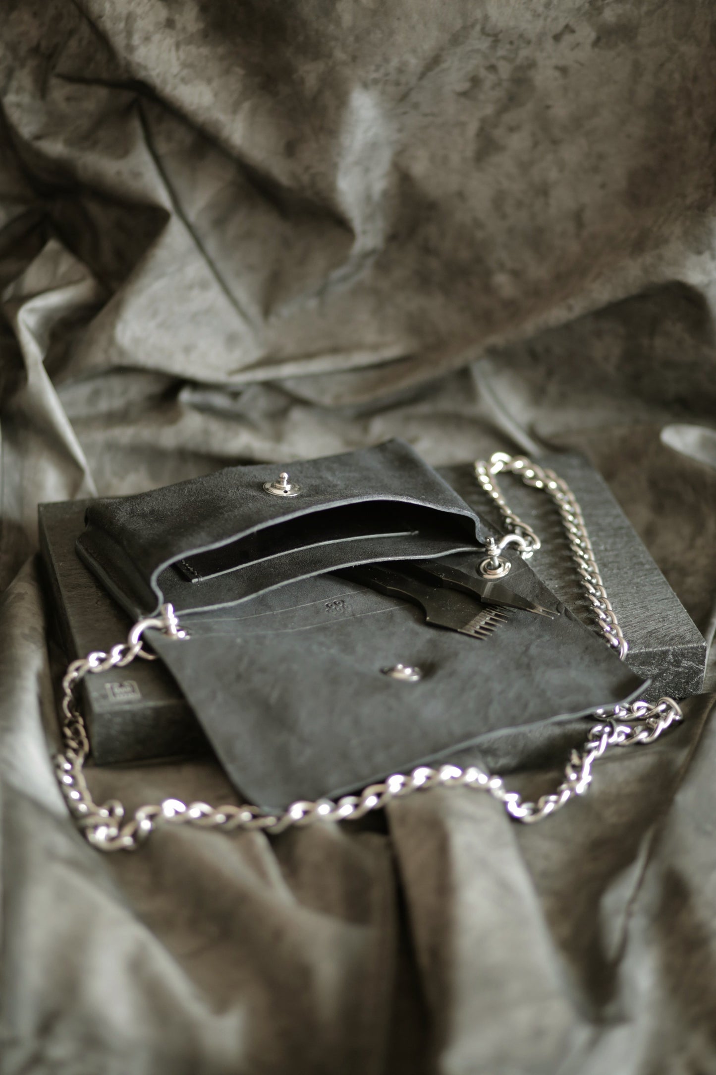 Köpenicker #004 black leather clutch with heavy polished steel strap and Loxx lock on textured background.