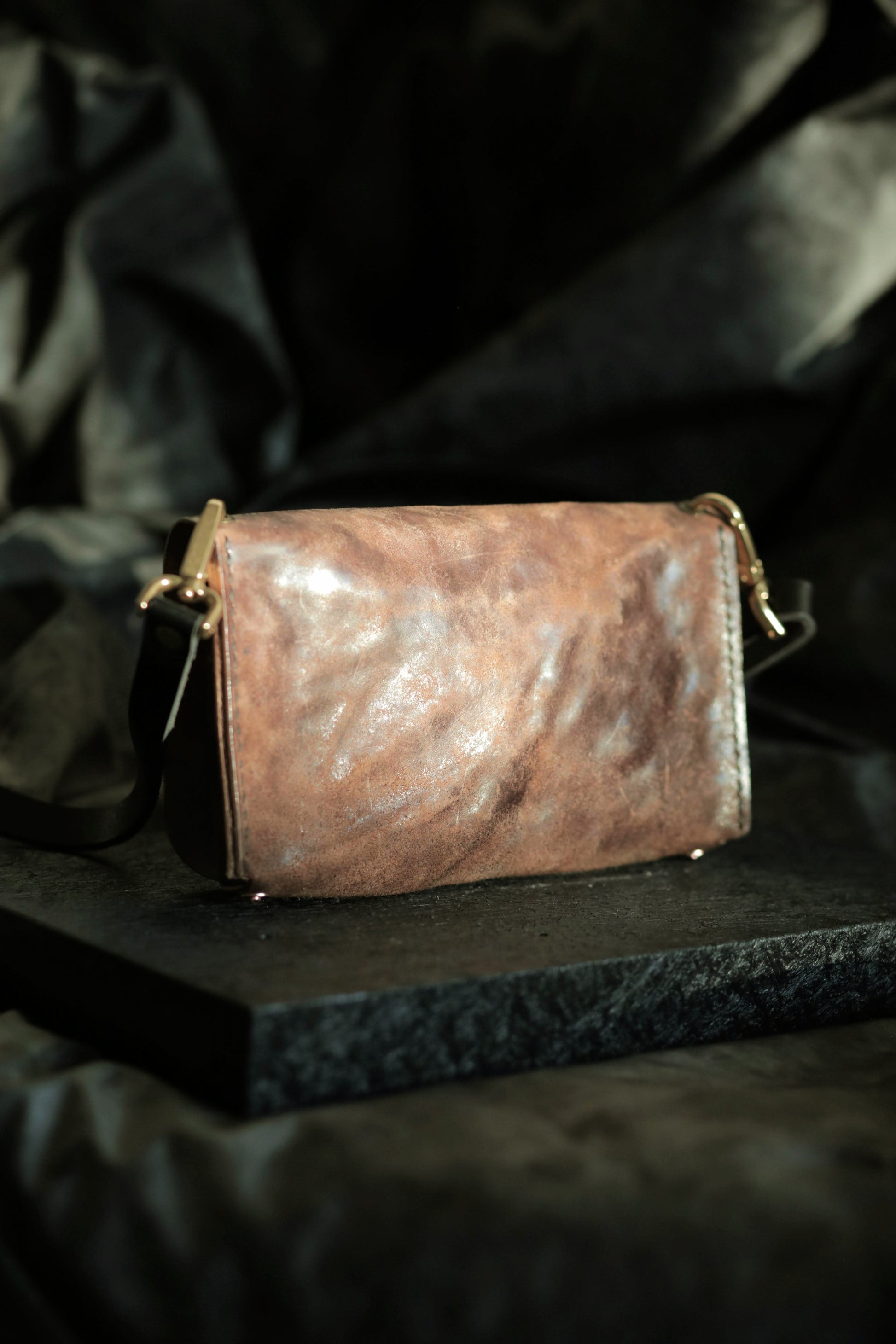 Köpenicker #003 brown bark leather clutch with brass hardware and adjustable strap on dark textured background.
