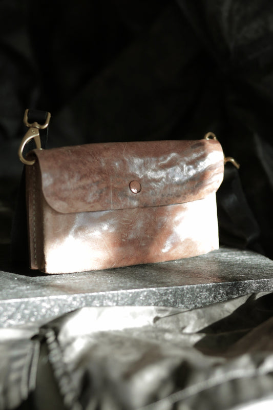 Köpenicker #002 prototype clutch in natural skin leather with copper button and adjustable shoulder strap on stone surface.