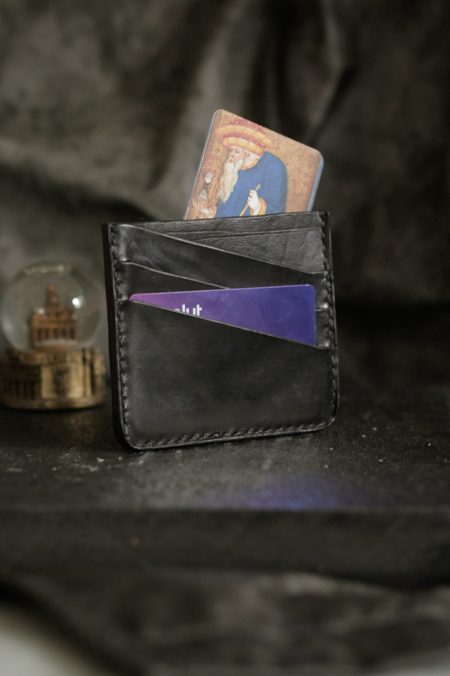 Schönlein #002 (sample) black leather culatta card holder with two cards in pockets on dark textured background.