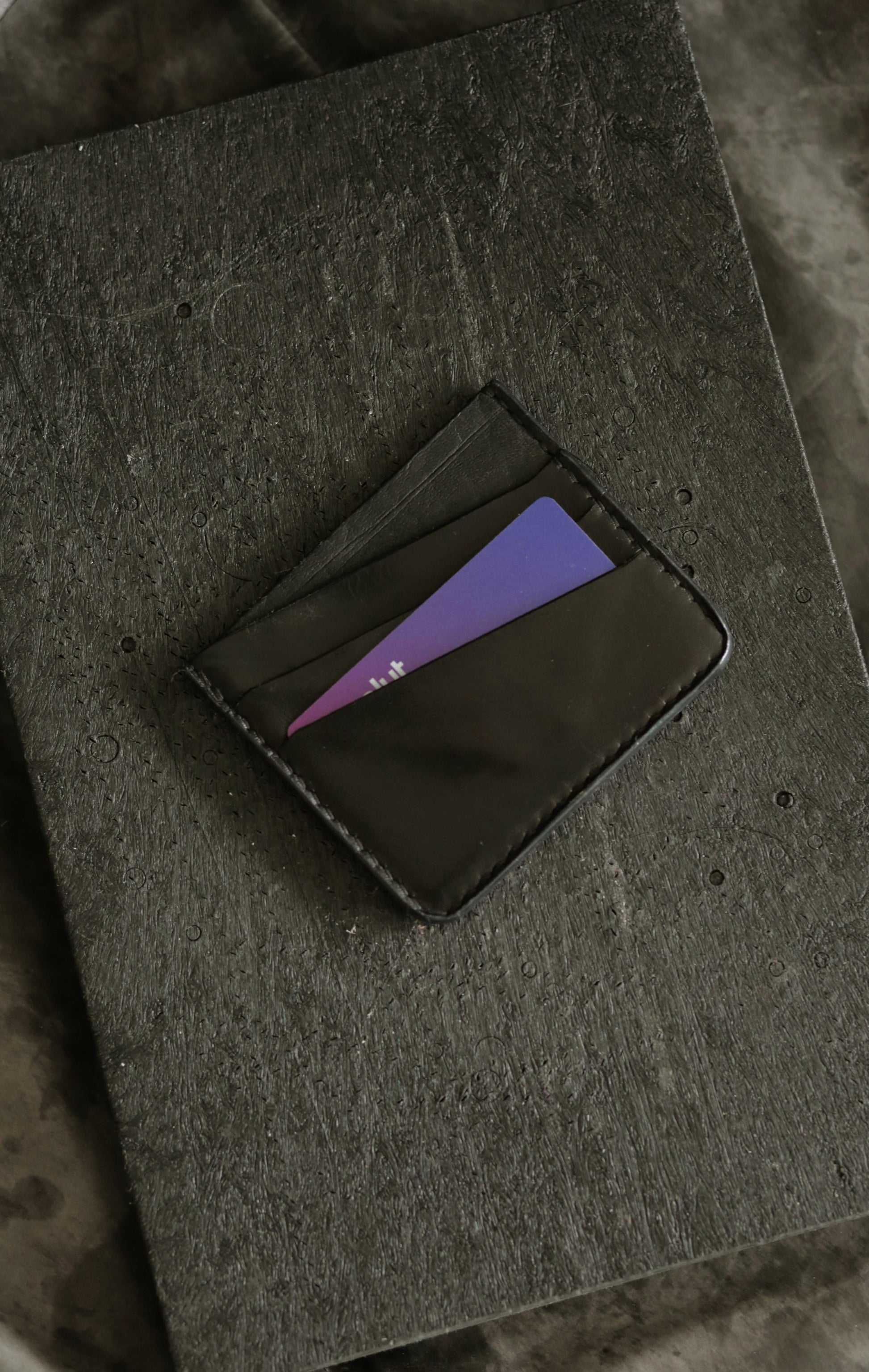 Schönlein #002 (sample) black veg tan leather culatta card holder with multiple card slots on textured surface.