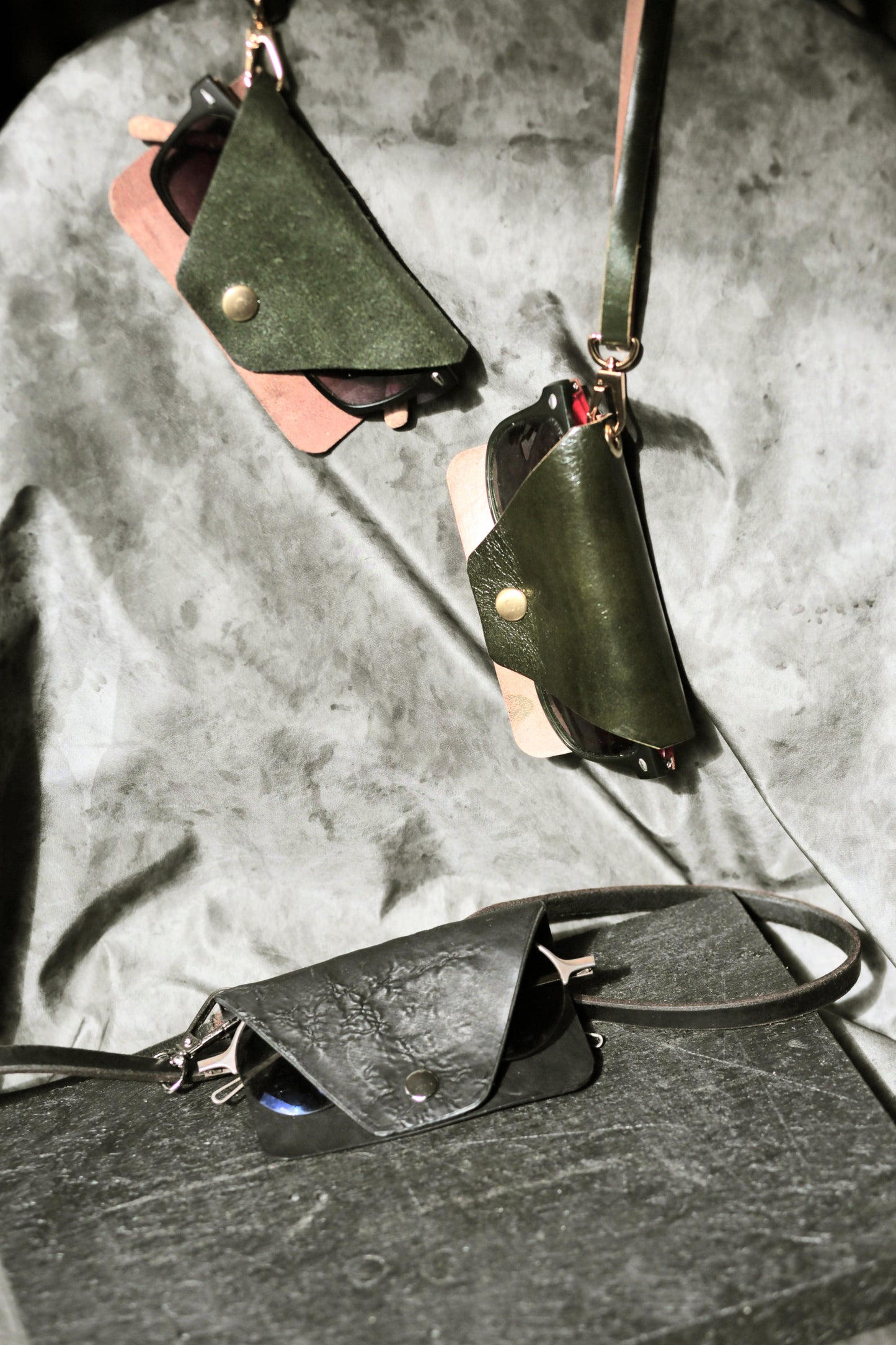 Green leather pouches with straps on a textured gray surface