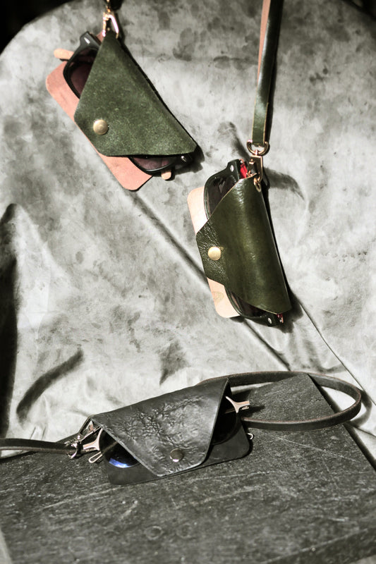 Green leather pouches with straps on a textured gray surface