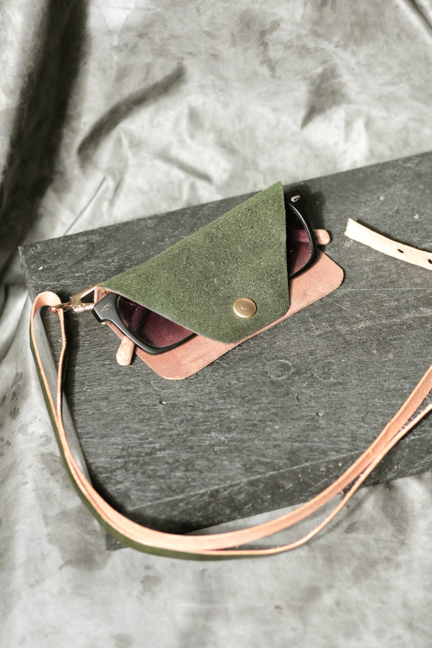 Sunglasses in a green case with a brown strap on a gray fabric background