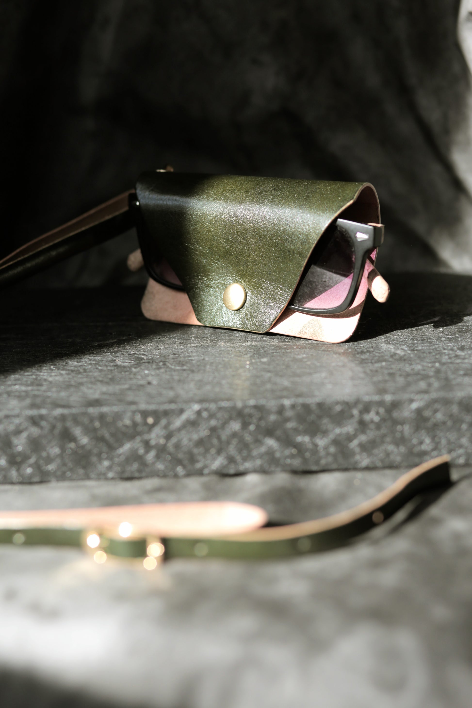 Green leather pouch with sunglasses on a textured surface