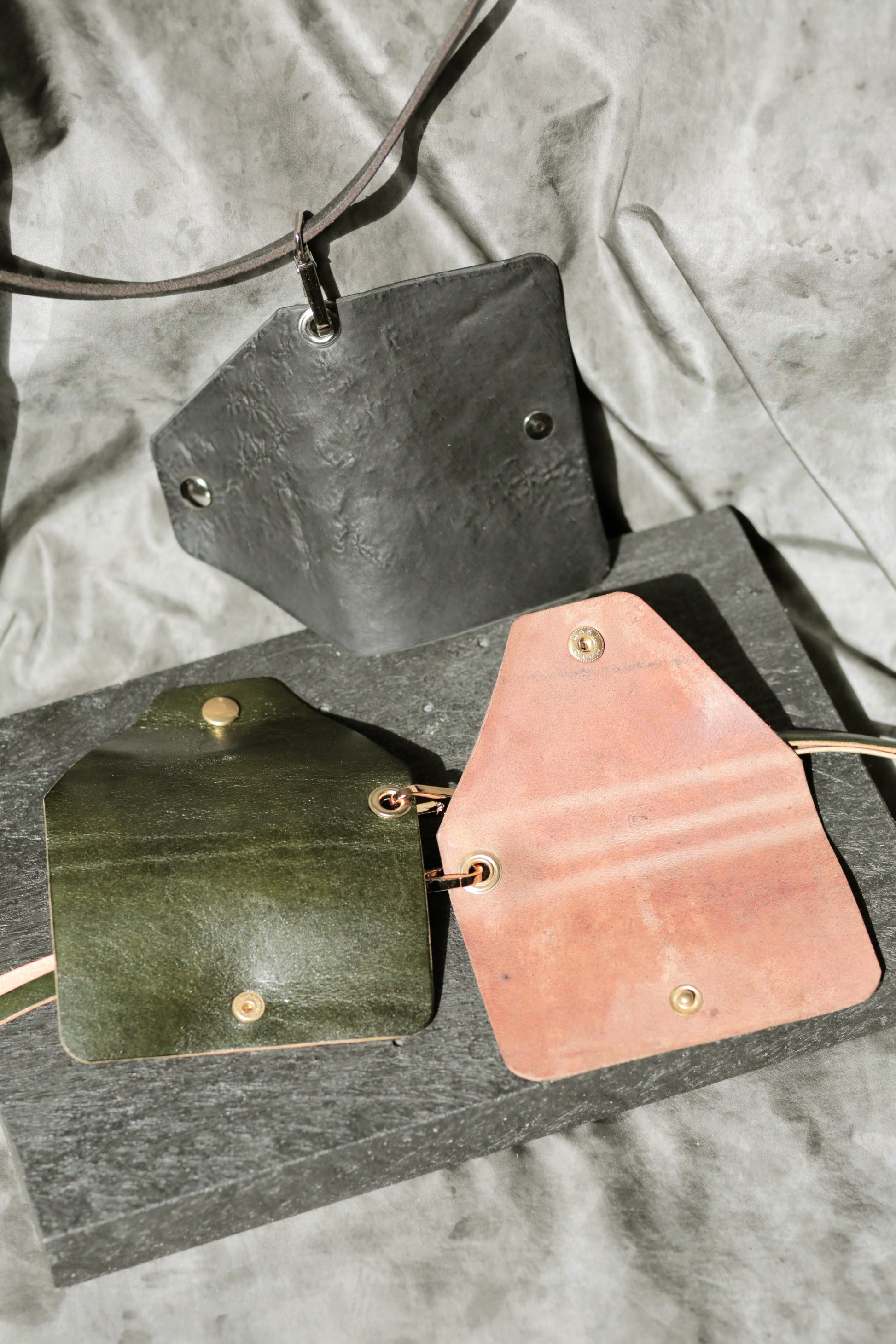 Three leather card holders in black, green, and pink on a gray fabric background.