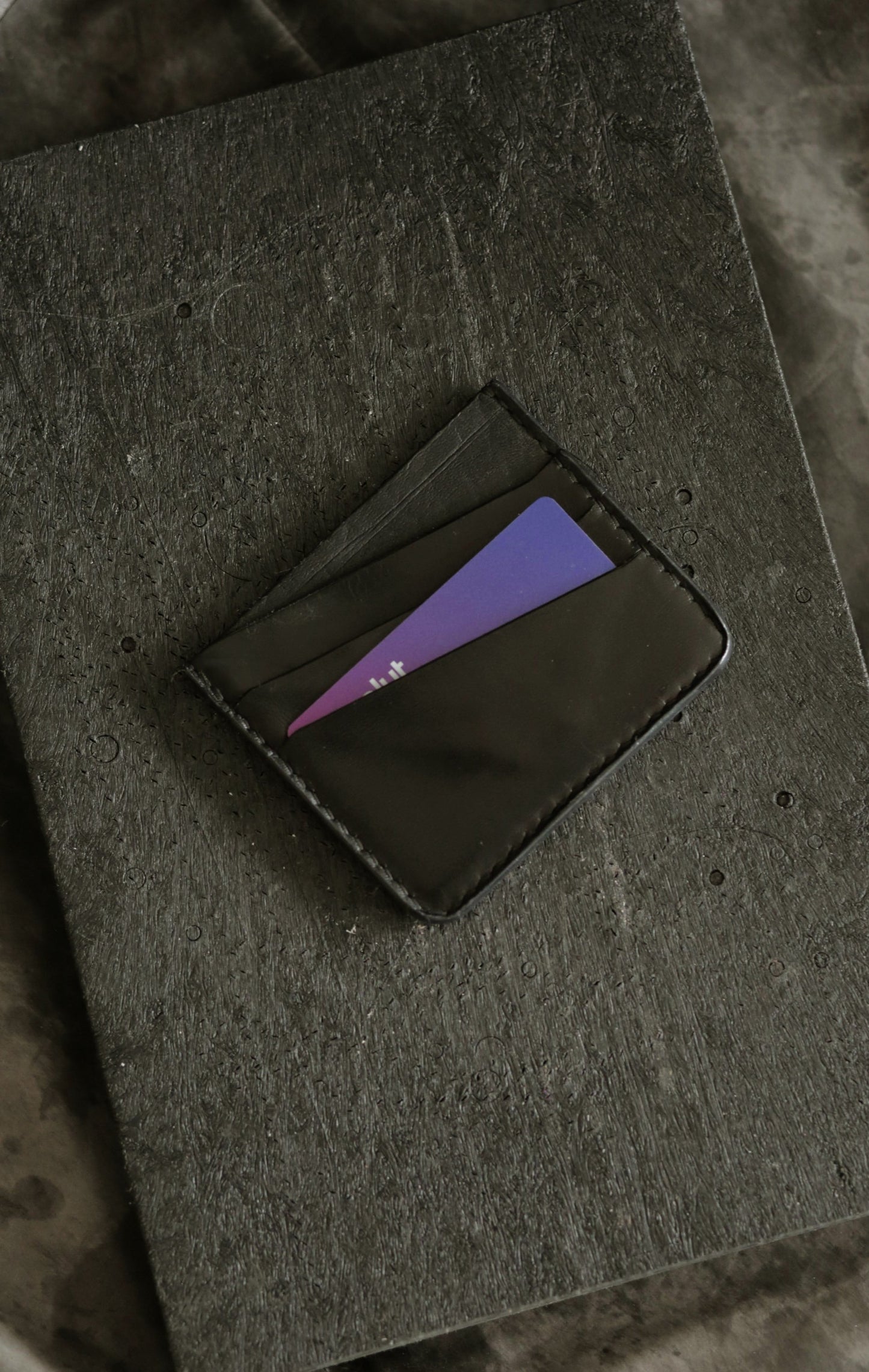 Schönlein #002 (sample) black veg tan leather culatta card holder with multiple card slots on textured surface.